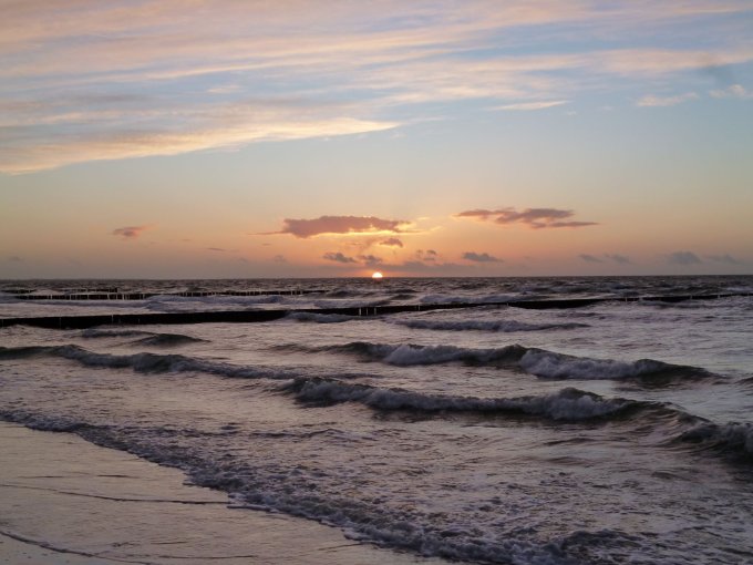 Ein Sonnenuntergang am Meer mit leichten Wellen und einen orangefarbenden Himmel.
